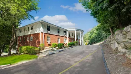 Front driveway leading to the entrance of The Manors Apartments, surrounded by lush greenery and mature trees.
