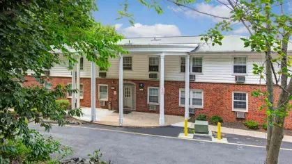 Front driveway leading to the entrance of The Manors Apartments, surrounded by lush greenery and mature trees.