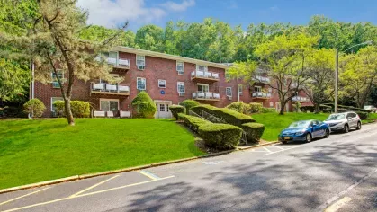 Street-facing view of The Manors Apartments with well-maintained grounds, outdoor balconies, and convenient parking, emphasizing the charm and accessibility of the community.