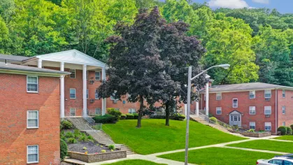 Exterior view of The Manors Apartments showcasing red brick buildings surrounded by lush greenery and mature trees, offering a peaceful and welcoming residential environment.