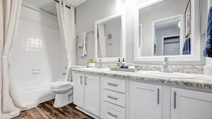 Contemporary bathroom with dual sinks, granite countertops, and a full-size bathtub at The Maxwell Apartments.