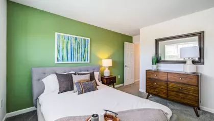 A serene bedroom with a green accent wall, soft bedding, and warm wooden furniture.
