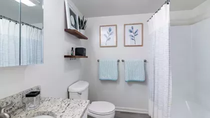 A clean, modern bathroom featuring granite countertops, blue accents, and framed artwork.