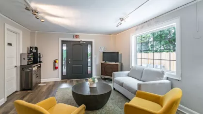 A cozy lounge with a gray sofa, yellow armchairs, and a coffee table in a bright, well-lit room.