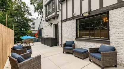 An outdoor patio area featuring cozy wicker chairs with blue cushions, a table with an umbrella, and a charming Tudor-style building in the background.