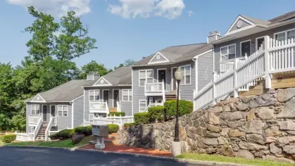 A residential complex with gray buildings, white railings, and landscaped surroundings.