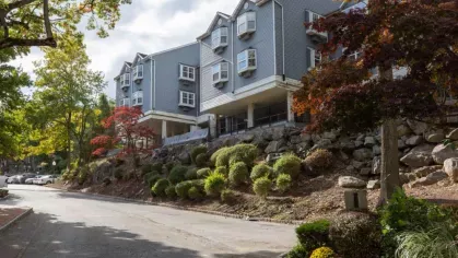 A side view of a residential building with lush greenery and a scenic road.