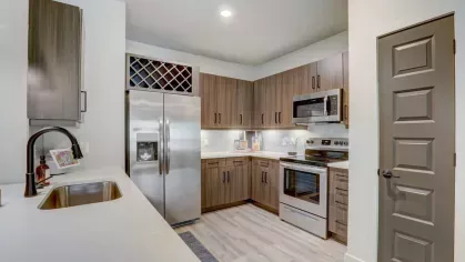 A fully equipped kitchen with sleek cabinetry, a wine rack, and stainless steel appliances in a Tropia Wellen Park apartment.