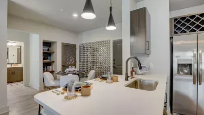 A fully equipped kitchen with sleek cabinetry, a wine rack, and stainless steel appliances in a Tropia Wellen Park apartment.