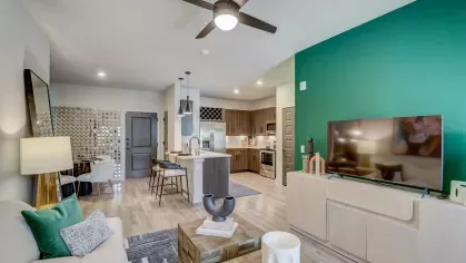A modern open-concept living room and kitchen with green accent walls, contemporary furniture, and stainless steel appliances at Tropia Wellen Park Apartments.