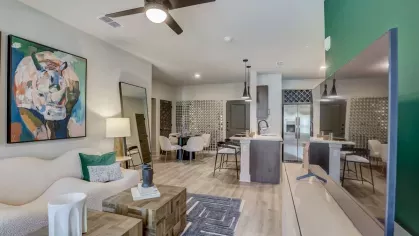 A modern open-concept living room and kitchen with green accent walls, contemporary furniture, and stainless steel appliances at Tropia Wellen Park Apartments.