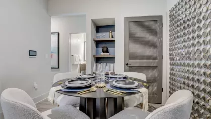 A beautifully set dining table with four chairs, a centerpiece, and modern decor, adjacent to open shelving and a unique wall accent.
