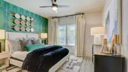 A stylish bedroom with a feature green wallpaper, a plush bed, and contemporary decor, illuminated by natural light.