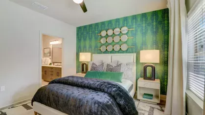 A stylish bedroom with a feature green wallpaper, a plush bed, and contemporary decor, illuminated by natural light.