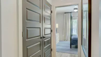 A hallway with double doors leading into a well-lit bedroom featuring neutral tones and inviting decor.
