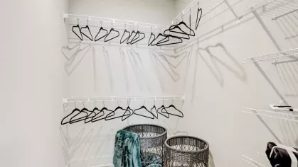 A large walk-in closet with wire shelving, wicker baskets, and black hangers, offering organized storage solutions.
