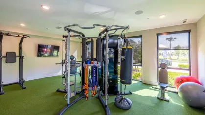 Image 1: Fitness center with modern exercise equipment, including a functional trainer, punching bag, and kettlebells, overlooking landscaped views through large windows.