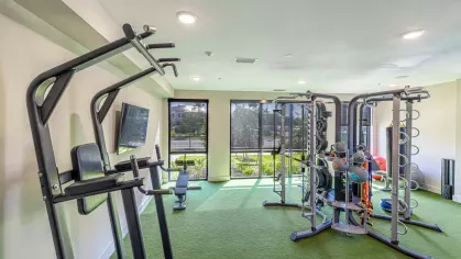 Image 1: Fitness center with modern exercise equipment, including a functional trainer, punching bag, and kettlebells, overlooking landscaped views through large windows.