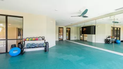 Image 1: Fitness center with modern exercise equipment, including a functional trainer, punching bag, and kettlebells, overlooking landscaped views through large windows.