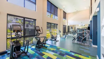 Image 1: Fitness center with modern exercise equipment, including a functional trainer, punching bag, and kettlebells, overlooking landscaped views through large windows.
