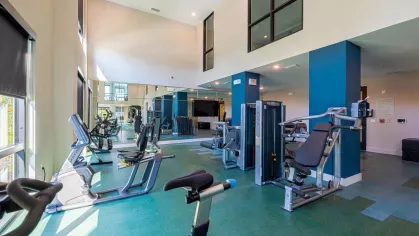 Image 1: Fitness center with modern exercise equipment, including a functional trainer, punching bag, and kettlebells, overlooking landscaped views through large windows.