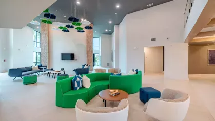 Image 5: Inviting community lounge with bold green and blue seating, modern decor, and ample space for gatherings at Tropia Wellen Park Apartments.