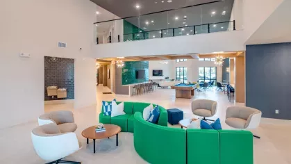 Image 5: Inviting community lounge with bold green and blue seating, modern decor, and ample space for gatherings at Tropia Wellen Park Apartments.