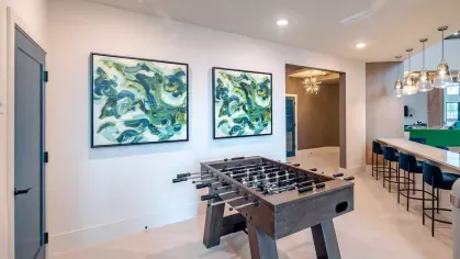 A foosball table area with vibrant abstract art and a nearby bar counter with sleek blue chairs for casual gatherings.