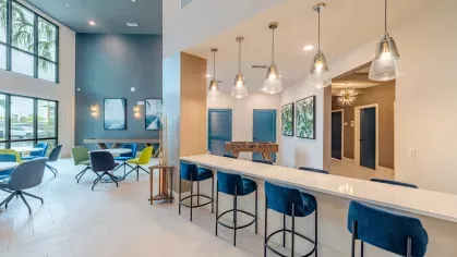 A vibrant coffee bar with tropical-themed wallpaper, illuminated by warm pendant lighting, offering a modern beverage station with snacks and refreshments.