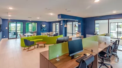 A spacious coworking area at Tropia Wellen Park Apartments featuring comfortable seating, private workstations, and large windows for natural light.