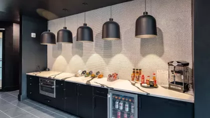 A snack bar with black cabinetry, modern lighting, and a variety of refreshments displayed on a countertop.