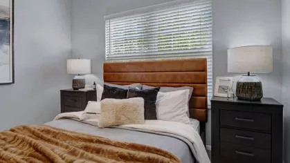 A stylish bedroom at Trotter's Landing Apartments with a plush, leather-upholstered bed, elegant black nightstands, and natural light pouring in through the window.