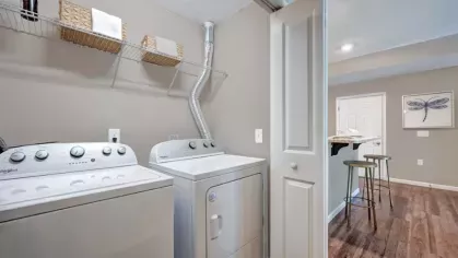 In-unit laundry area with washer and dryer at Walden Lakes Apartments, conveniently located with storage shelving above and easy access to the living space.