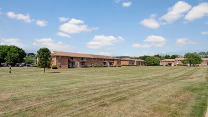Expansive green lawn with brick apartment buildings at Washington Gardens Apartments in Washington, NJ, surrounded by a clear blue sky and scenic views.