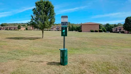 Convenient pet waste station situated on the spacious grounds of Washington Gardens Apartments, with brick apartment buildings visible in the background.