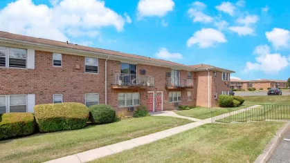 Sidewalks leading to brick apartment buildings at Washington Gardens Apartments, surrounded by well-maintained landscaping and a sunny sky.