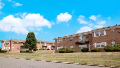 Brick apartment buildings with green lawns and clear blue skies at Washington Gardens Apartments, offering a serene suburban living environment.