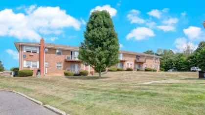 Brick apartment buildings with green lawns and clear blue skies at Washington Gardens Apartments, offering a serene suburban living environment.