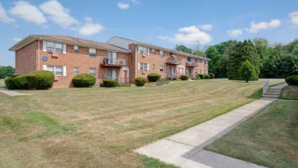 Brick apartment buildings with green lawns and clear blue skies at Washington Gardens Apartments, offering a serene suburban living environment.