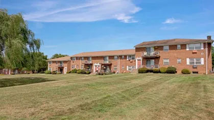 Expansive green lawn with brick apartment buildings at Washington Gardens Apartments in Washington, NJ, surrounded by a clear blue sky and scenic views.