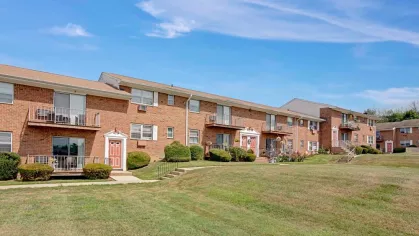 Expansive green lawn with brick apartment buildings at Washington Gardens Apartments in Washington, NJ, surrounded by a clear blue sky and scenic views.