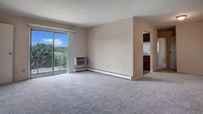 Spacious living room with neutral carpeting, sliding glass doors leading to a private balcony, and plenty of natural light at Washington Gardens Apartments in Washington, NJ.