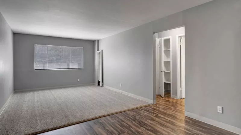 Spacious living room with a mix of carpet and hardwood flooring, featuring a large window that brings in natural light.
