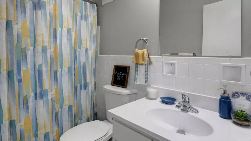 Bright and modern bathroom with a white vanity, tiled backsplash, and colorful shower curtain.