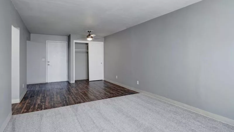 Spacious living room with a mix of carpet and hardwood flooring, featuring a large window that brings in natural light.