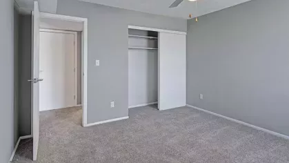 A cozy bedroom in a Wilson Plaza apartment featuring neutral carpet, a ceiling fan, and a spacious closet.