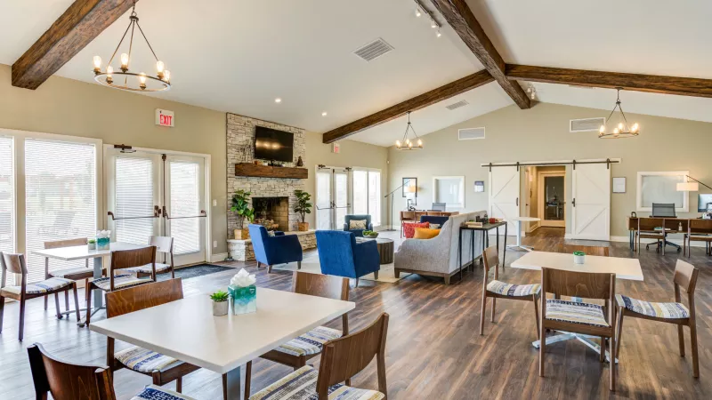 "Modern clubhouse at Worthington Meadows Apartments featuring cozy seating, a fireplace, and natural light from large windows."