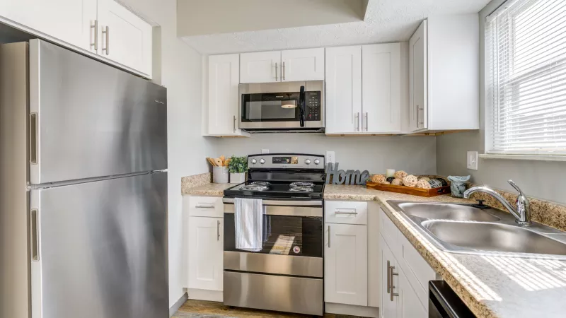 Fully equipped kitchen featuring stainless steel appliances, white cabinetry, and ample countertop space in Worthington Meadows Apartments.