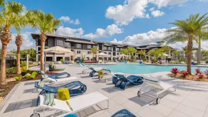 A vibrant pool deck with palm trees, lounge chairs, and umbrellas, creating a tropical atmosphere at Tropia Wellen Park Apartments.