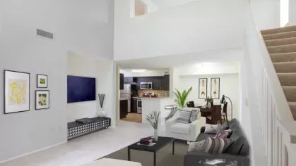 A spacious loft-style living room with high ceilings, a modern staircase, an open kitchen with stainless steel appliances, and a cozy seating area with stylish décor.